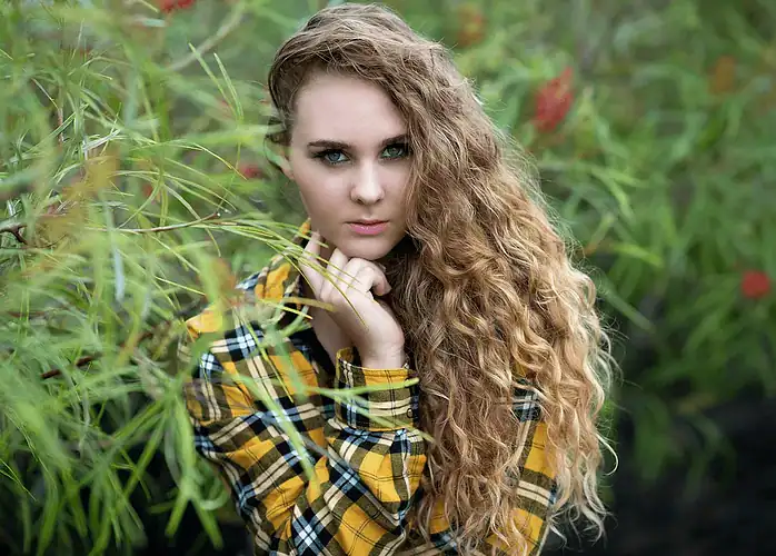 Elegant portrait of a woman with long flowing hair standing in front of lush greenery