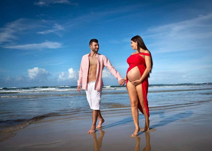 Husband and pregnant wife walking hand-in-hand on the beach