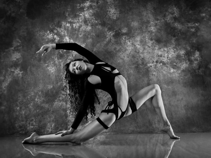 Studio portrait of gymnast performer in extreme stretch pose wearing black outfit, athletic photography