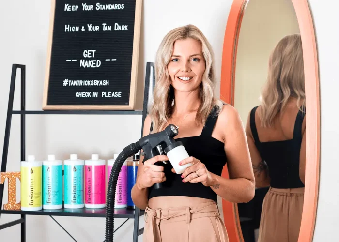 Tanning professional holding a spray tanning gun in a studio setting