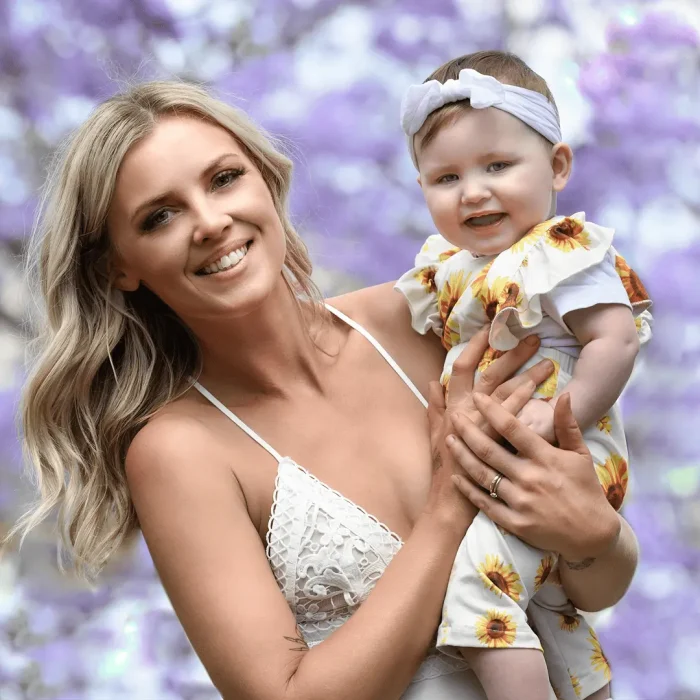 Happy mother holding her baby under blooming jacaranda trees
