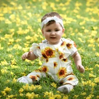 Baby sitting on grass among yellow flowers