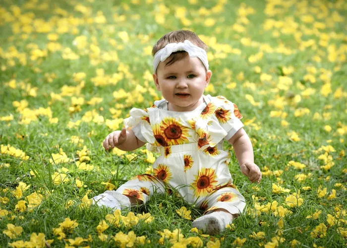 Baby sitting on grass among yellow flowers