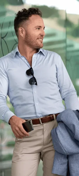 Commercial fashion portrait of a man holding a phone in one hand, a jacket in the other, with sunglasses hanging from his shirt
