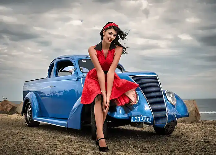 Glamour portrait of a woman in a red dress posing in front of a blue classic car