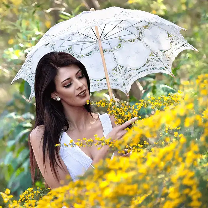 Glamour portrait of a woman behind yellow flowers holding a white umbrella