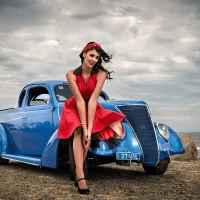 Lady in red dress leaning on an old blue car