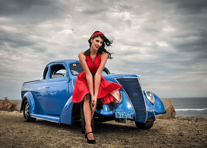 Lady in red dress leaning on an old blue car