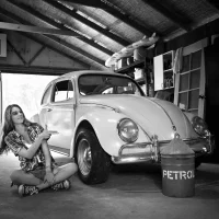 Black-and-white portrait of a lady sitting next to a VW Beetle