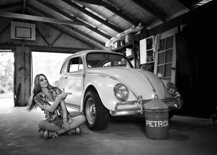 Black-and-white portrait of a lady sitting next to a VW Beetle