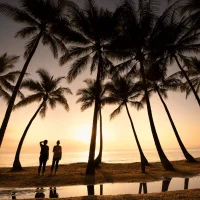 Couple standing separately at sunset in Port Douglas with palm trees and water reflections