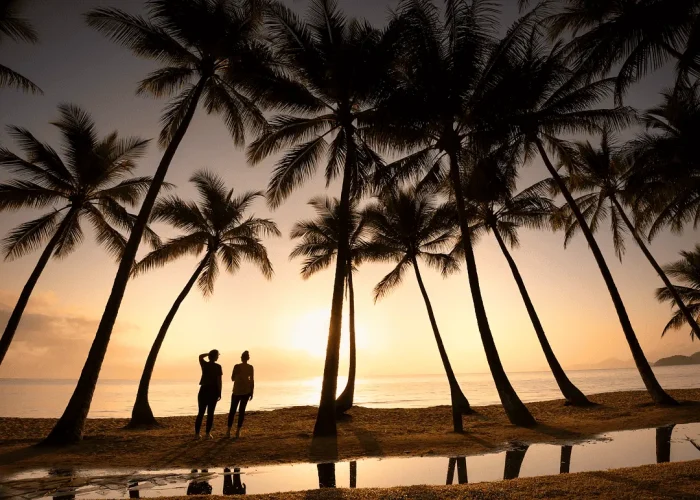 Couple standing separately at sunset in Port Douglas with palm trees and water reflections