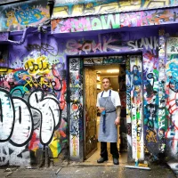 Shop owner standing in a graffiti-covered laneway doorway in Melbourne
