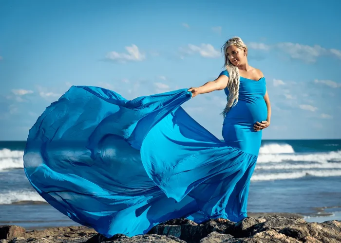 Pregnant woman walking on the beach wearing a blue flowing dress