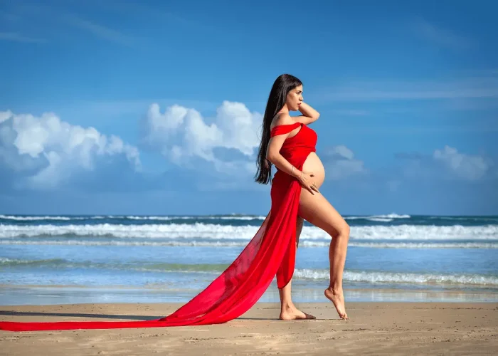 Pregnant woman walking on the beach wearing a red flowing dress