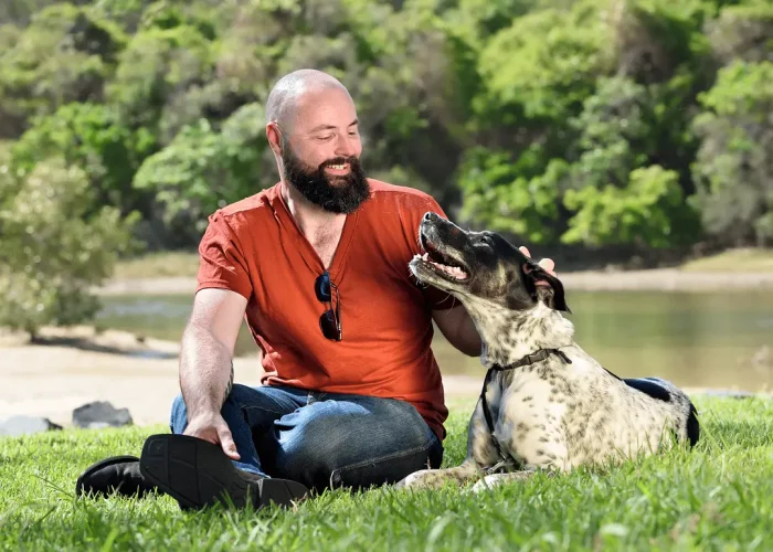 Man sitting on the ground next to his dog, smiling