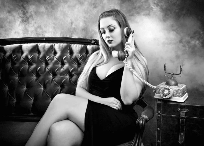 Black-and-white studio portrait of a lady on a lounge using an old telephone
